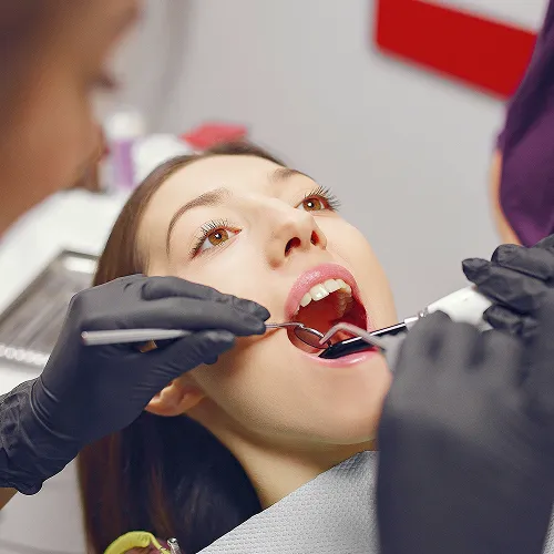 Gloved hands using dental tools in woman's mouth.