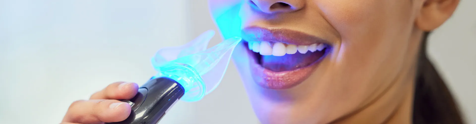 Woman shining whitening led light on her smile.