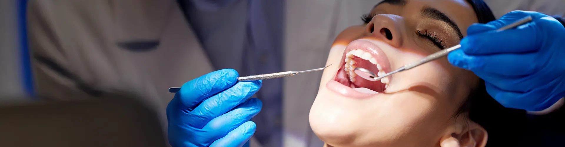 Gloved hands using dental tools in woman's mouth.