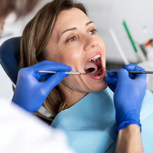 Gloved hands using dental tools in woman's mouth.
