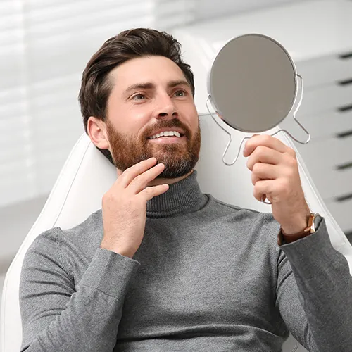man smiling into hand mirror