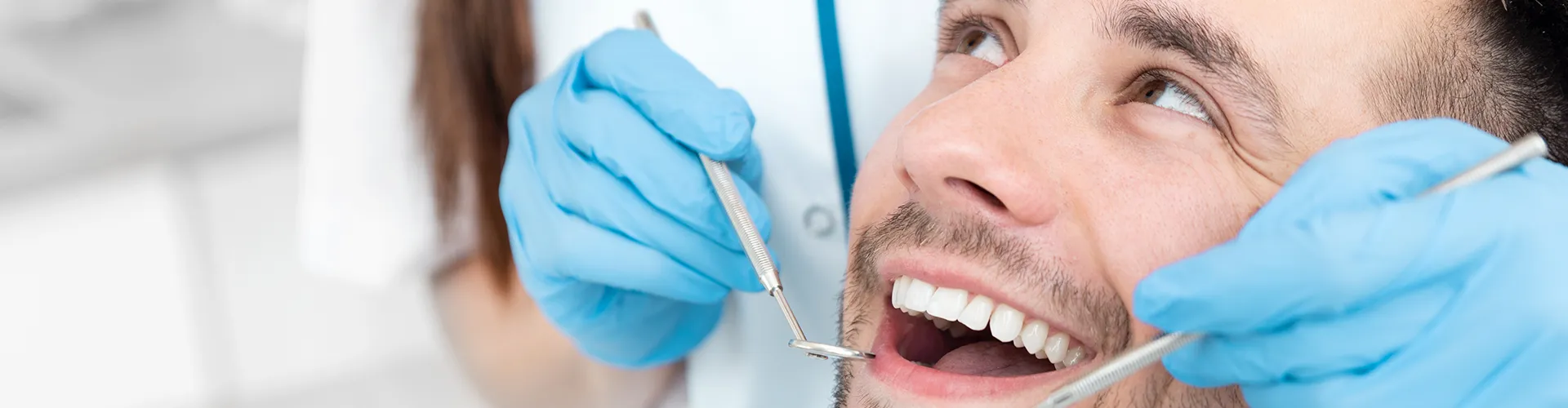 gloved hands holding dental tools beside smiling man's mouth