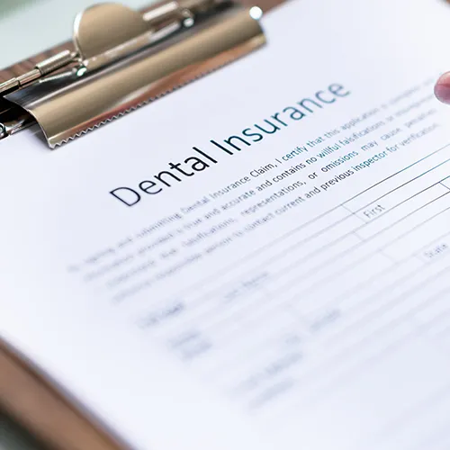 hand with pen filling out dental form besie large tooth model