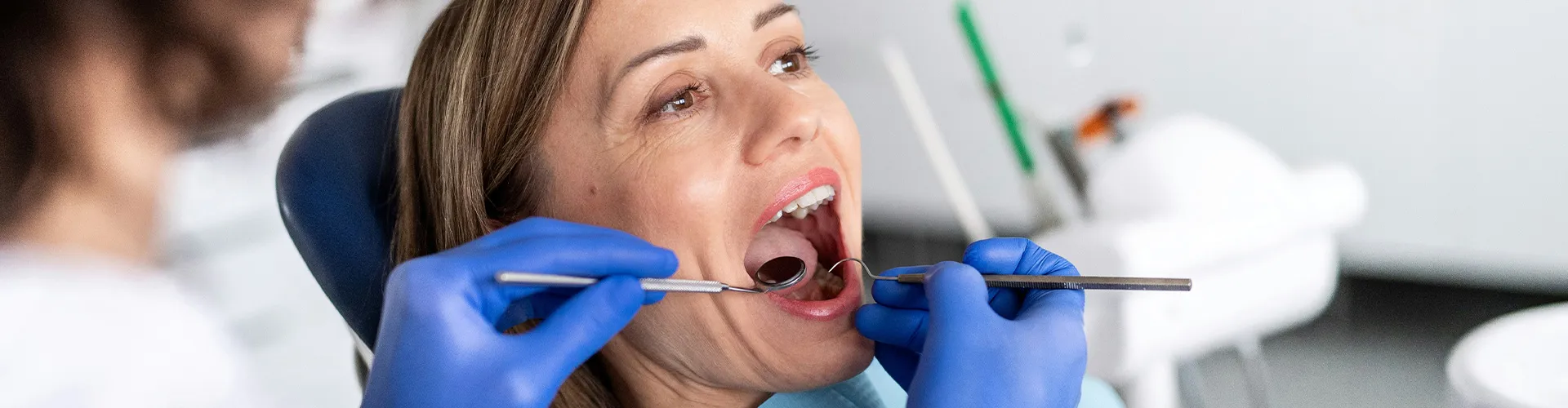 Gloved hands using dental tools in woman's mouth.