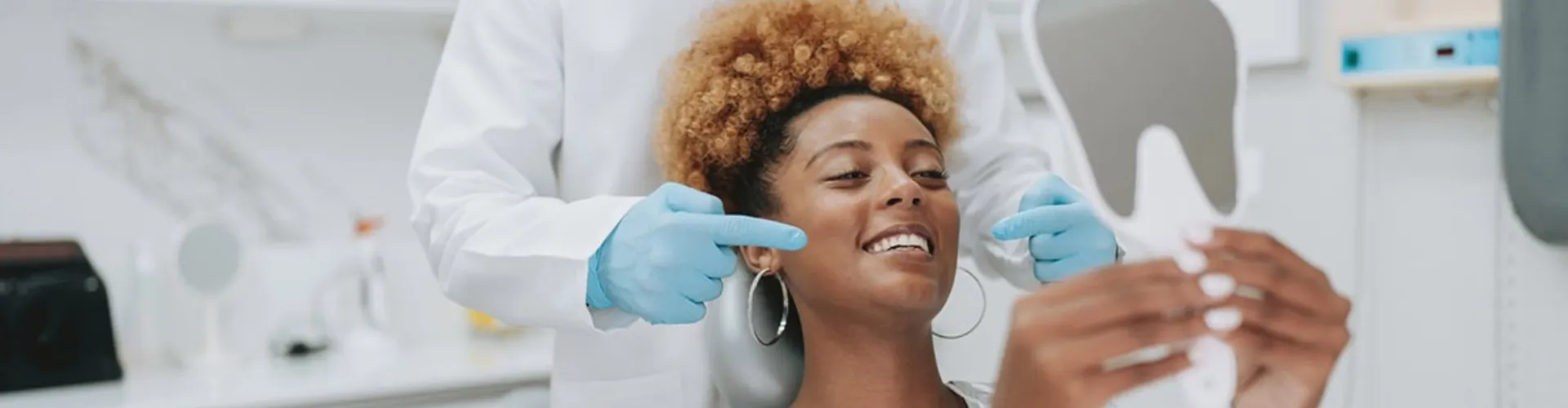Male dentist pointing at female patient smiling into hand mirror.