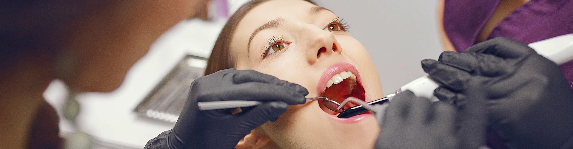 Gloved hands using dental tools in woman's mouth.