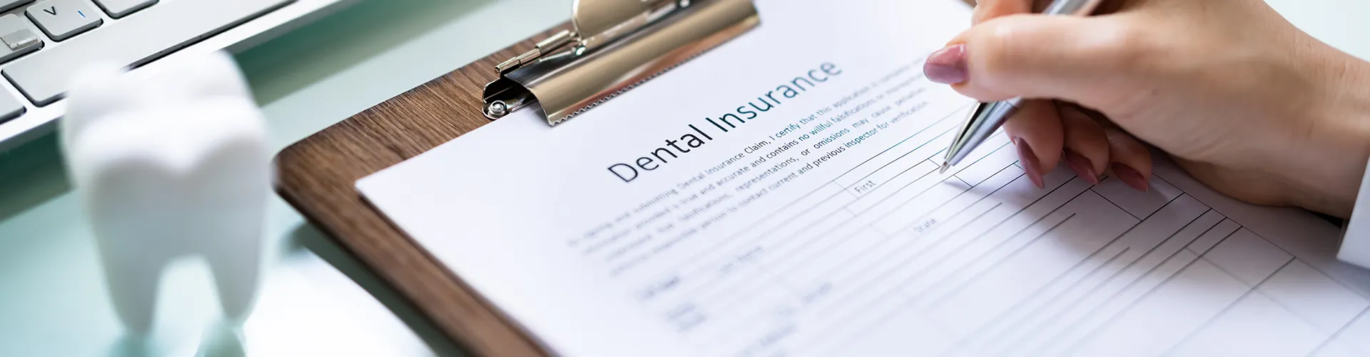 hand with pen filling out dental form besie large tooth model