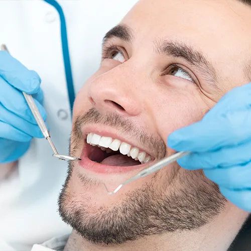 gloved hands holding dental tools beside smiling man's mouth