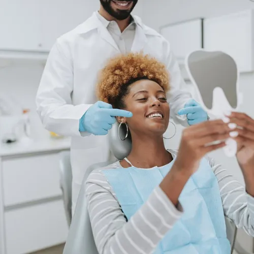 Male dentist pointing at female patient smiling into hand mirror.