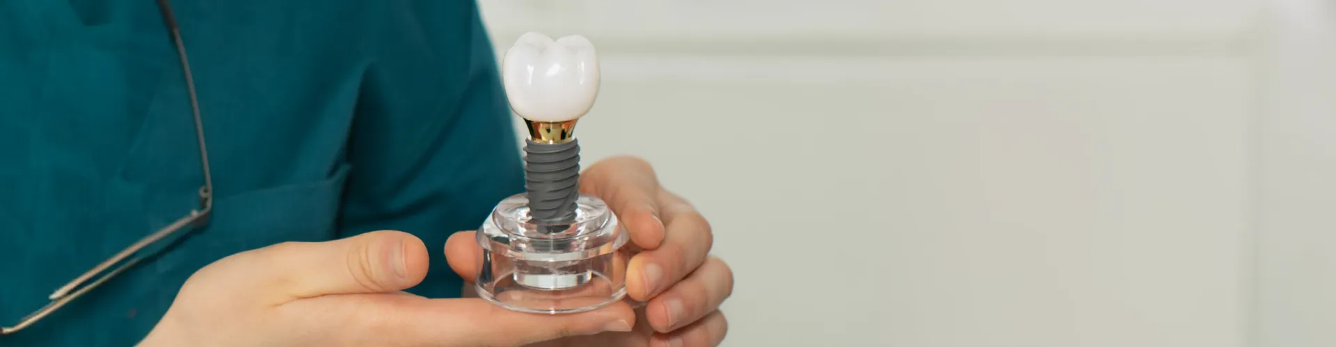 Dentist holding a dental implant model with a titanium post and ceramic crown, demonstrating how dental implants replace missing teeth with a natural-looking, permanent restoration.