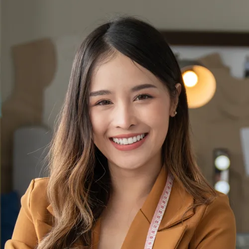 Smiling woman wearing a brown blazer and measuring tape around her neck.
